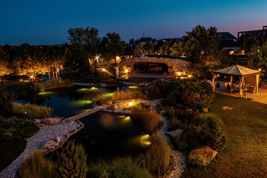 Courtyard of country house with patio and artificial pond with lighting on a summer evening.