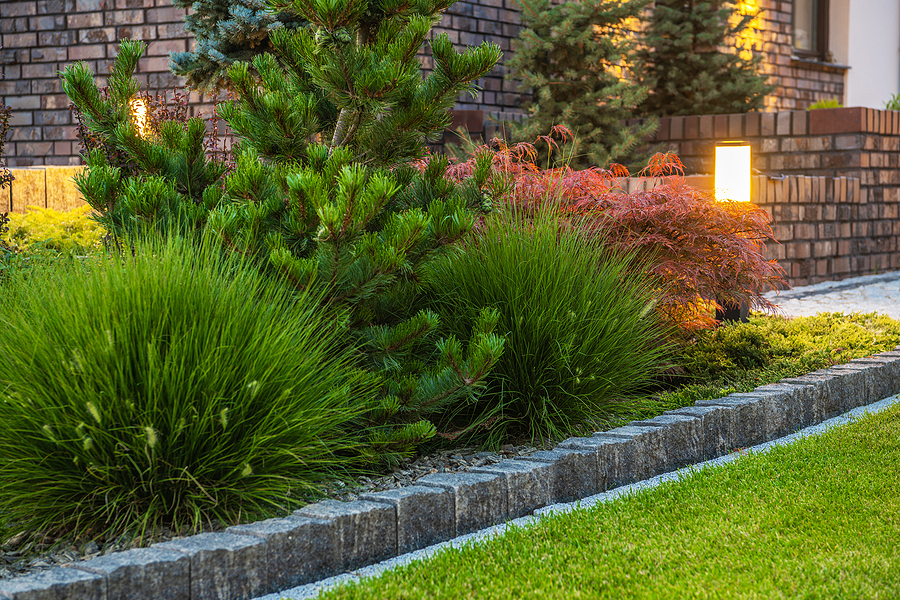 Residential garden bed with shrubbery and greenery lighted by lantern posts.